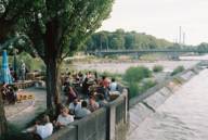 Am Ufer der Isar sitzen mehrere Personen im Kulturstrand in München und genießen das gute Wetter.