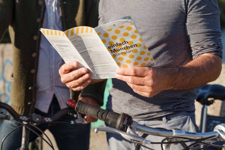 Ein Mann mit Fahrrad hält einen München-Prospekt in der Hand.